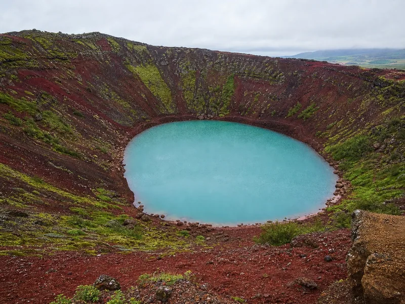 Der rote Schlackenrand und das grüne Wasser des Kerið-Kraters